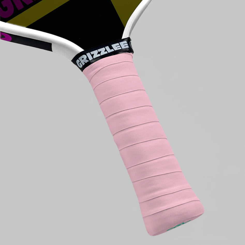 Close-up of a light pink pickleball paddle overgrip grip with 'Grizzlee' branding on a gray background