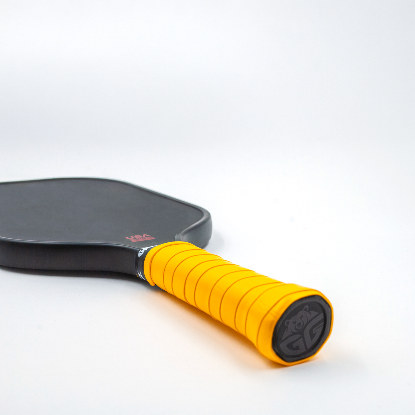 Neon Orange grizzlee Gripz wrapped around a paddle handle thats laying flat on a white surface - Premium Pickleball Overgrip by Grizzlee Gripz