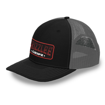 Black and grey snap back trucker hat embroidered badge logo on the front of a heat rising badge by Grizzlee Gripz